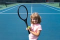 Funny kid tennis player on tennis court. Child boy with tennis racket and tennis balls.