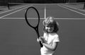 Funny kid tennis player on tennis court. Child boy with tennis racket and tennis balls.