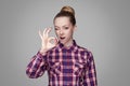 funny kissing beautiful girl with pink checkered shirt, collected bun hairstyle and makeup standing and showing Ok sign and