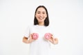 Funny korean woman posing with two delicious glazed doughnuts on chest, laughing and smiling, eats junk food, tasty