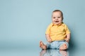 Funny laughing loud infant baby boy toddler in blue jeans and yellow shirt is sitting on the floor at free copy space