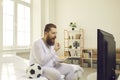 Funny lazy fat sports fan in pyjamas sitting on bed and watching football match on television Royalty Free Stock Photo