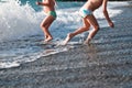 Funny legs of a girl and boy on the beach run away and jump into the sea waves at sunset