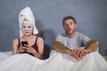 Eccentric and weird housewife with makeup facial mask and towel using mobile phone in bed and husband in desperate face expression