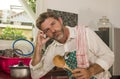 Funny lifestyle portrait of mid adult unhappy and stressed man in kitchen apron feeling frustrated and upset overwhelmed by Royalty Free Stock Photo