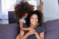 Little black girl hug smiling mom on couch from behind Royalty Free Stock Photo