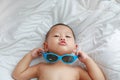 Funny little Asian baby boy with sunglasses lying on white blanket on bed. Above view Royalty Free Stock Photo