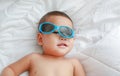 Funny little Asian baby boy with sunglasses lying on white blanket on bed. Above view Royalty Free Stock Photo