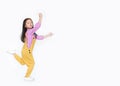 Funny little Asian child girl in pink-yellow dungarees jumping over white background with copy space. Freedom kid movement concept