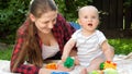 Funny little baby boy with mother lying on green grass at backyard garden and playing toys Royalty Free Stock Photo