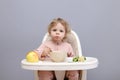 Funny little baby girl eating healthy food while sitting in high chair chewing soup looking at camera with curios facial Royalty Free Stock Photo