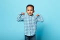 Funny little black boy showing biceps and smiling at camera, male child demonstrating his power and strength