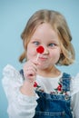 Funny little blonde girl in jeans overalls looking at lollipop candy over blue Royalty Free Stock Photo