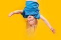 Funny little blonde girl upside-down on bright yellow background. Child topsy-turvy. Copy space Royalty Free Stock Photo