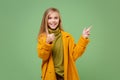 Funny little blonde kid girl 12-13 years old in yellow coat posing isolated on pastel green background. Childhood Royalty Free Stock Photo