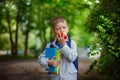 Funny little boy with books and backpack, eating apple on gree Royalty Free Stock Photo