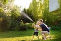 Funny little boy with his father playing with garden hose in sunny backyard