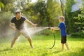 Funny little boy with his father playing with garden hose in sunny backyard. Preschooler child having fun with spray of water. Royalty Free Stock Photo