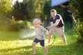 Funny little boy with his father playing with garden hose in sunny backyard. Preschooler child having fun with spray of water