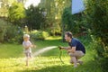 Funny little boy with his father playing with garden hose in sunny backyard. Preschooler child having fun with spray of water