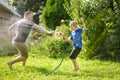 Funny little boy with his father playing with garden hose in sunny backyard. Preschooler child having fun with spray of water. Royalty Free Stock Photo