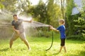 Funny little boy with his father playing with garden hose in sunny backyard. Preschooler child having fun with spray of water. Royalty Free Stock Photo