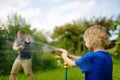 Funny little boy with his father playing with garden hose in sunny backyard. Preschooler child having fun with spray of water.