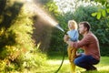 Funny little boy with his father watering plants and playing with garden hose in sunny backyard. Preschooler child having fun with Royalty Free Stock Photo