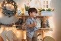 Funny little boy opening glass jar with sweets standing on wooden shelf in kitchen