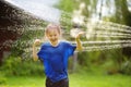 Funny little boy playing with garden sprinkler in sunny backyard. Preschooler child laughing, jumping and having fun with spray of Royalty Free Stock Photo