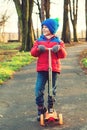 Funny little boy riding scooter in city park in cold autumn. Kids sports outdoors. Autumn and winter fashion. Happy child playing Royalty Free Stock Photo