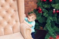 Funny little boy standing near sofa and Christmas tree with colorful xmas ball Royalty Free Stock Photo