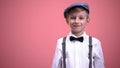 Funny little boy in vintage clothes smiling on camera against pink background