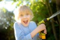 Funny little boy watering plants and playing with garden hose with sprinkler in sunny backyard. Preschooler child having fun with Royalty Free Stock Photo