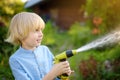 Funny little boy watering plants and playing with garden hose with sprinkler in sunny backyard. Preschooler child having fun with Royalty Free Stock Photo