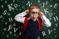 Funny child with glasses and letters near chalkboard. Speech therapy concept