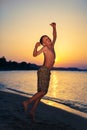 Funny little child jumping on beach at sunset.