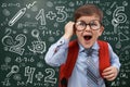 Funny child wearing glasses near chalkboard with mathematical equations. First time at school