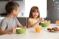 Funny little children having breakfast and drinking citrus juice at home