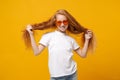 Funny little ginger kid girl 12-13 years old in white t-shirt heart glasses isolated on bright yellow wall background Royalty Free Stock Photo