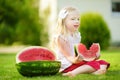 Funny little girl biting a slice of watermelon outdoors on warm and sunny summer day Royalty Free Stock Photo