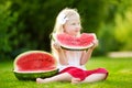 Funny little girl biting a slice of watermelon outdoors on warm and sunny summer day Royalty Free Stock Photo