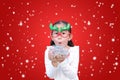 Funny little girl blowing a multi color paper spray in her hands against floating snow on red christmas background. A moment of Royalty Free Stock Photo