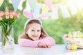 Funny little girl in bunny ears at breakfast on Easter morning at table with Easter eggs Royalty Free Stock Photo