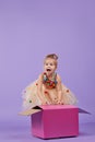 A funny little girl child in a magnificent holiday dress look inside a large gift colored box,