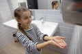 Little girl in the bathroom dries her hands with a hand dryer