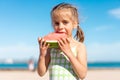 Funny little girl eat watermelon sunny summer day at ocean beach. Cute caucasian female child enjoy summer fruit bite slice of Royalty Free Stock Photo