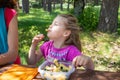 Funny little girl eating pasta from a plastic box next to her mother in a table picnic in countryside Royalty Free Stock Photo