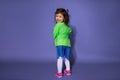 Funny little girl in football uniform stands with her back on purple background and looks into the frame