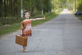 Funny little girl hitchhiker with a suitcase and a teddy bear. Travel.